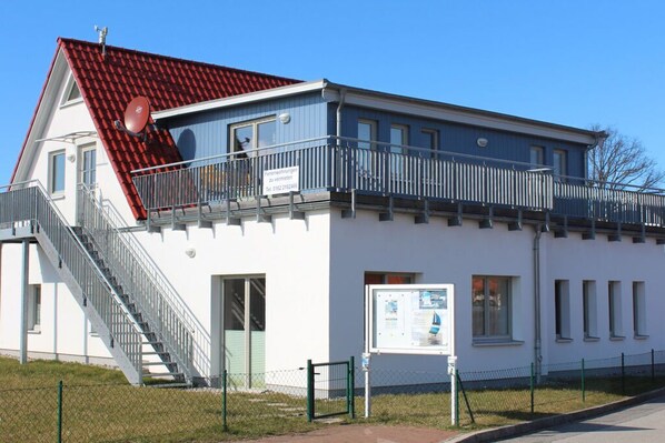 A building with a red-tiled roof, a balcony with a metal railing, and a staircase leading to the entrance.