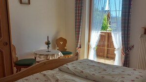 A bedroom with a bed, a chair, a small table, and a window with curtains. - Ferienwohnung Ulrichshögl (Ainring)