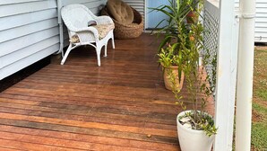 A wooden porch with two wicker chairs, a wicker basket, and a potted plant. - Memory Lane Accommodation (Tamborine Mountain)
