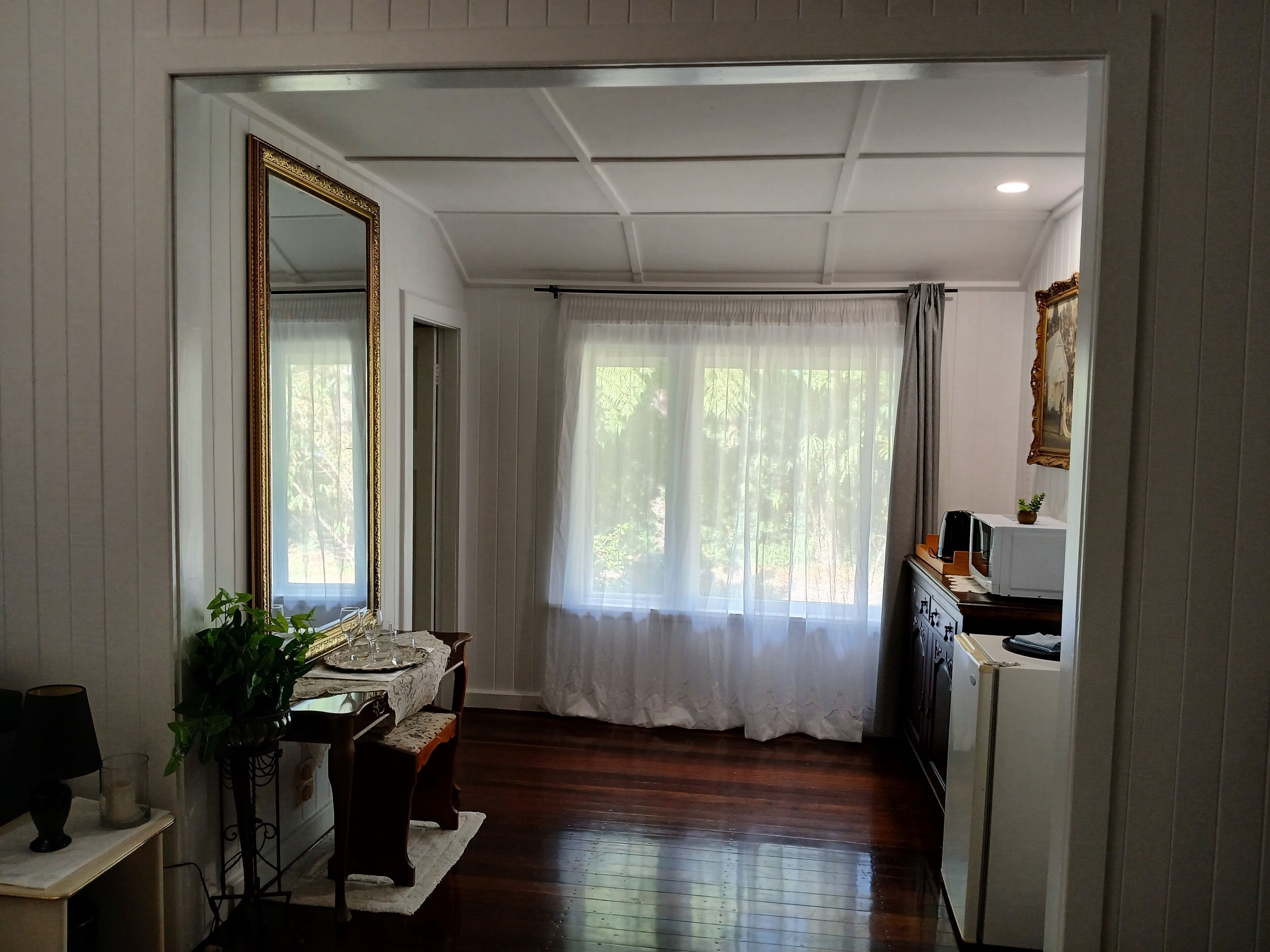 A room with a dining table, chairs, a mirror, a cabinet, and a window with curtains.