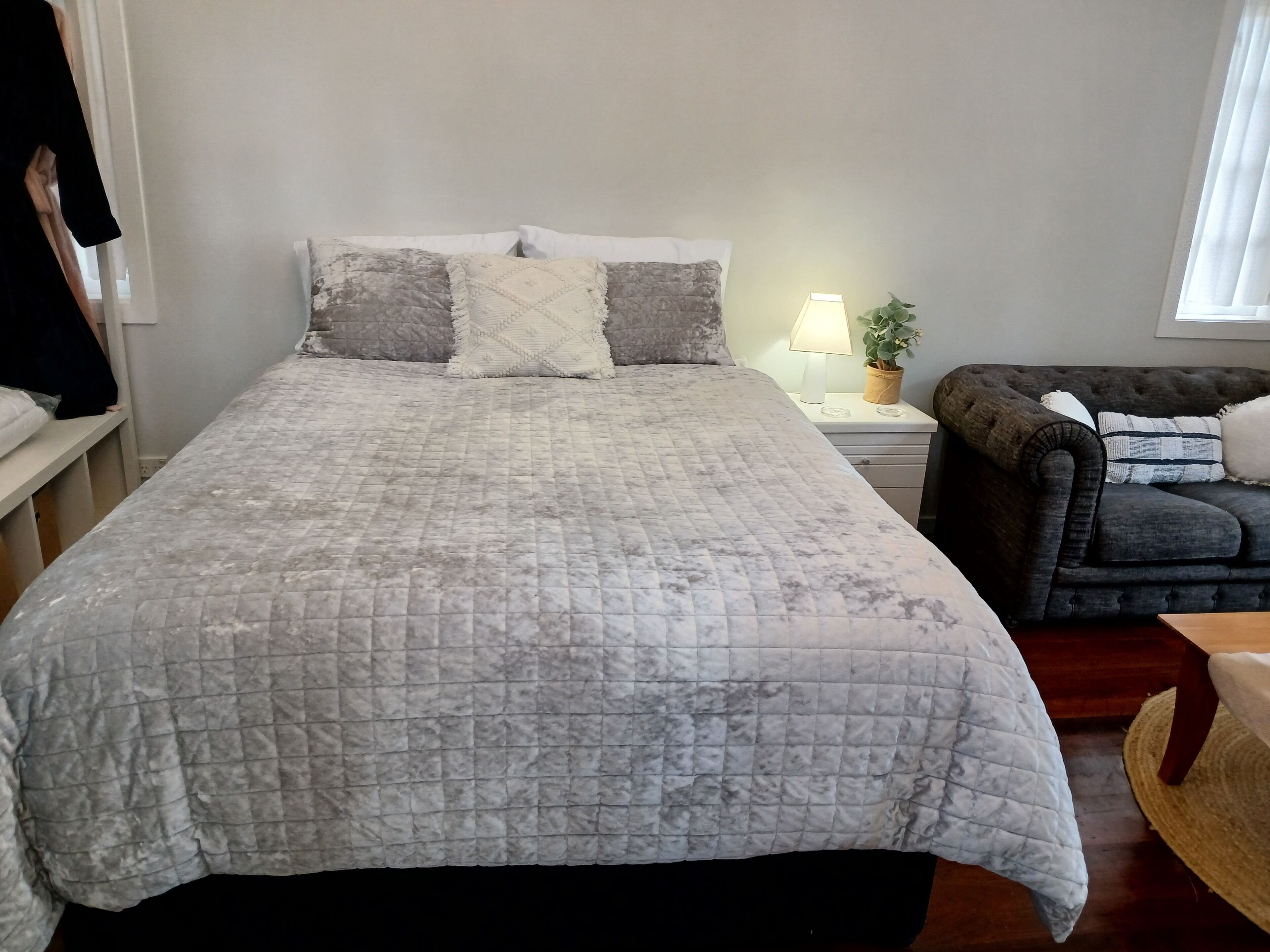 A bedroom with a bed, a nightstand, a lamp, a potted plant, and a sofa.