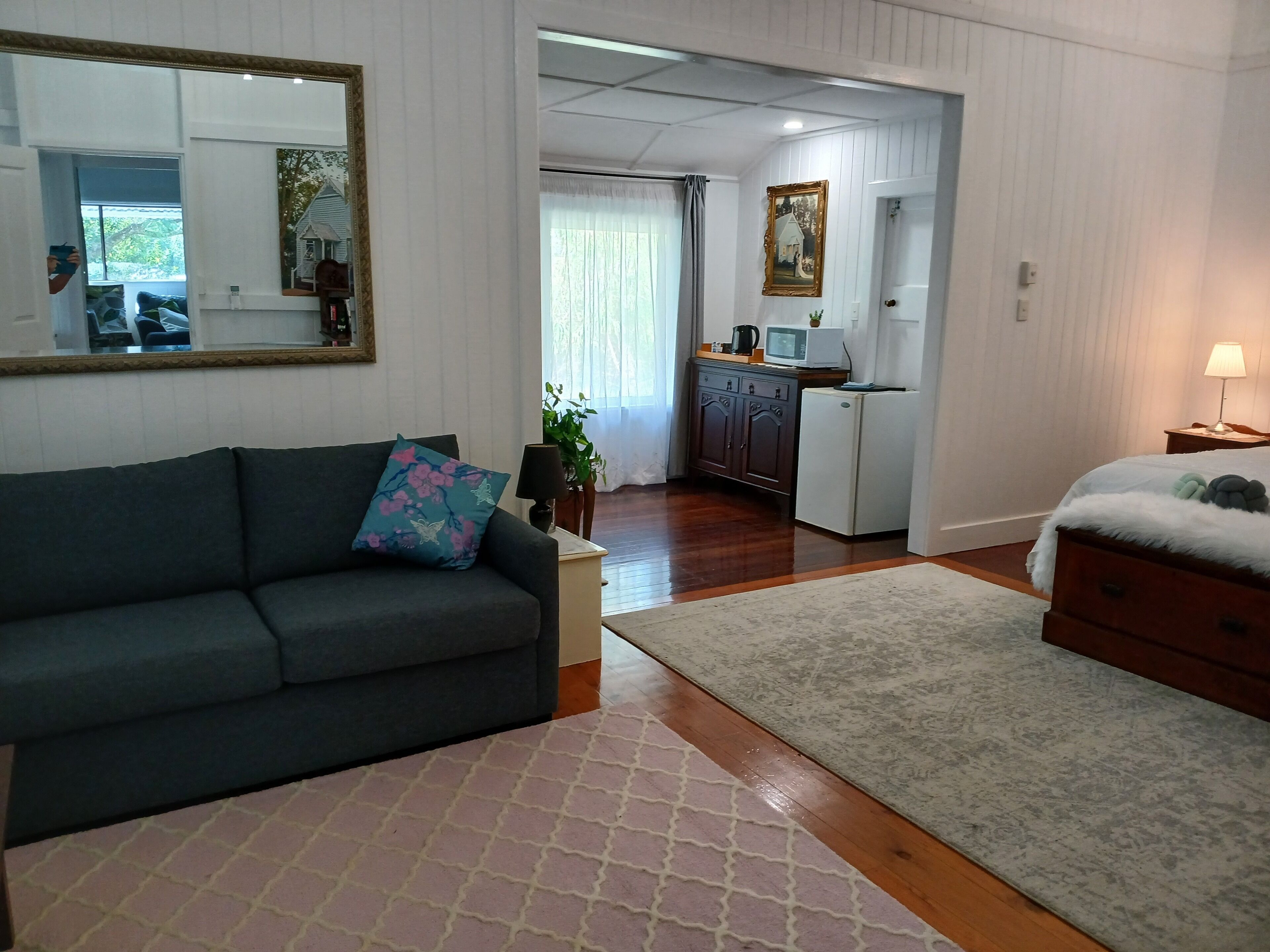 A living room with a sofa, a coffee table, a rug, a dresser, and a kitchen area with a refrigerator and microwave.