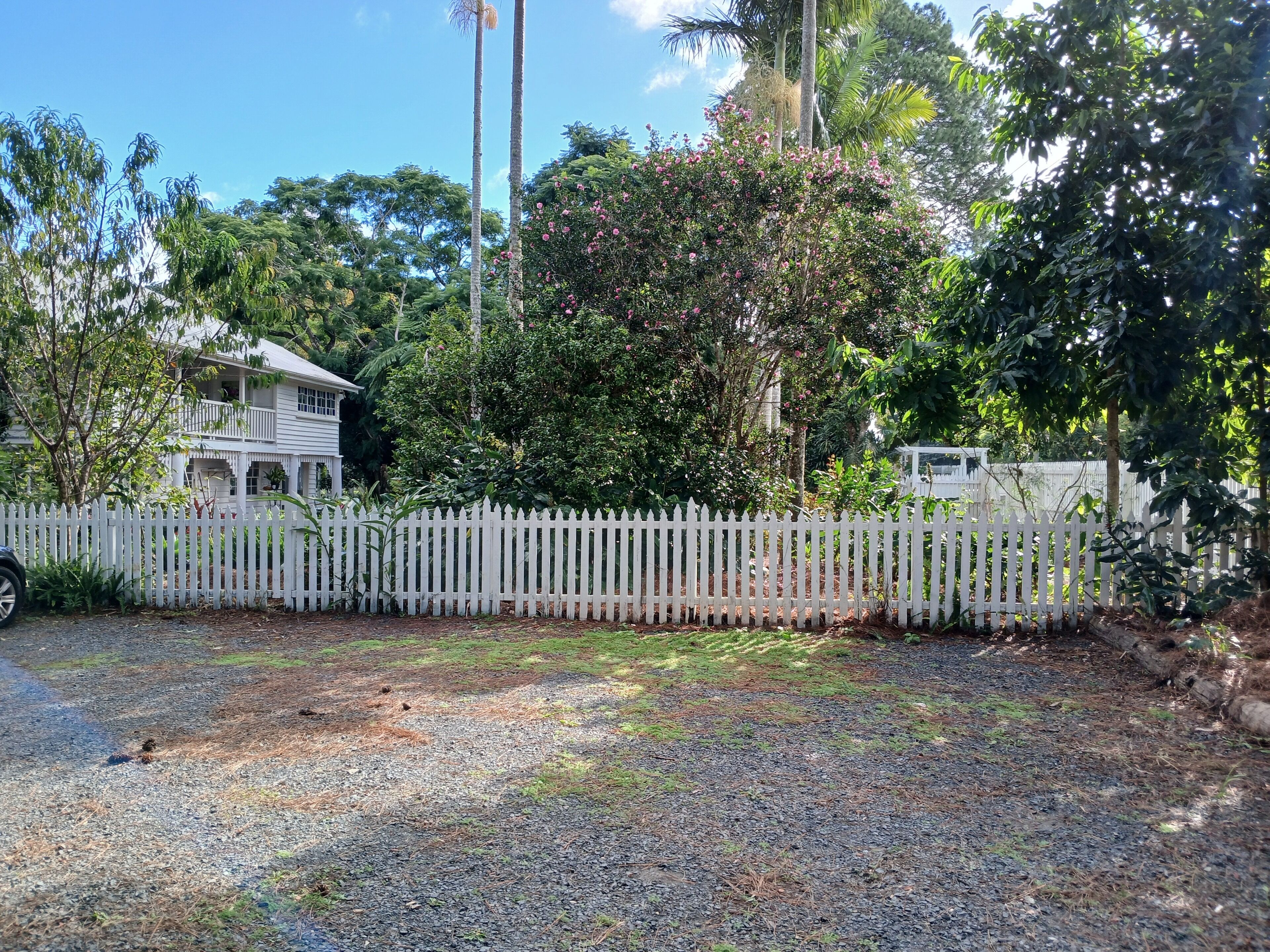 A white picket fence, a gravel driveway, and a house with a balcony.