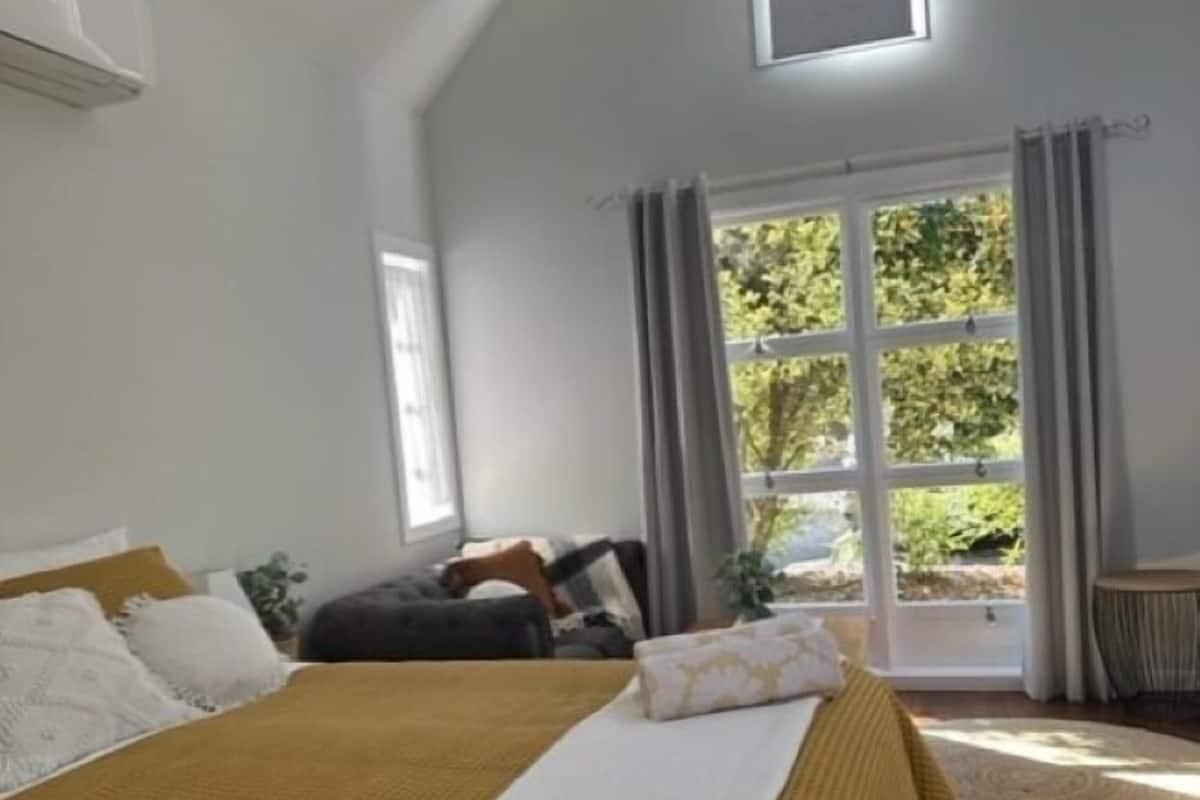 A bedroom with a large bed, a skylight, a view of greenery outside, and a modern chandelier.