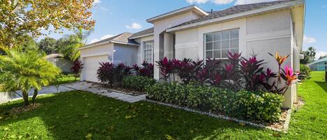 A single-story house with a well-maintained lawn and a variety of colorful plants in the front yard.
