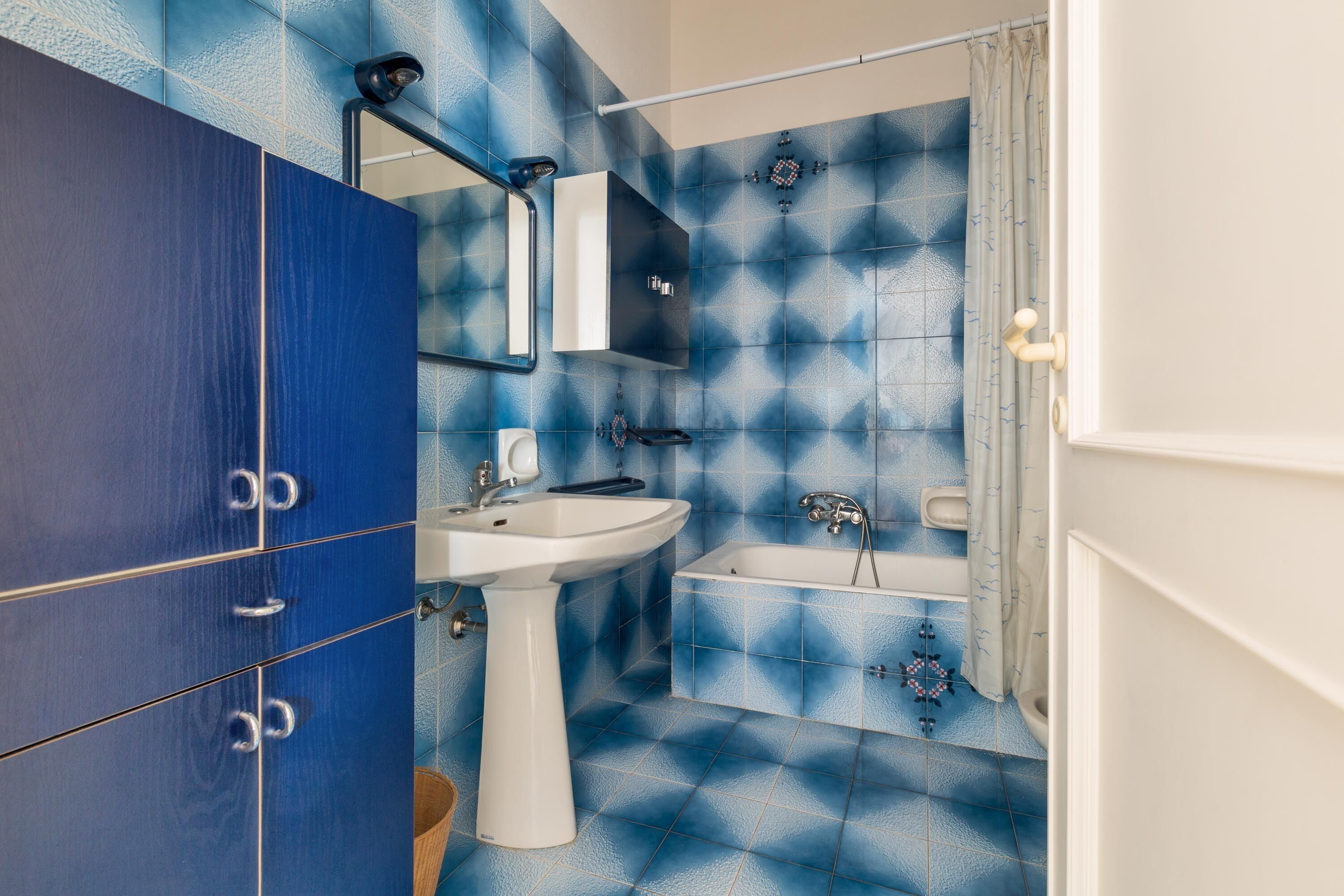 Une salle de bain avec un sol carrelé de bleu, un lavabo blanc, une baignoire et un meuble bleu.