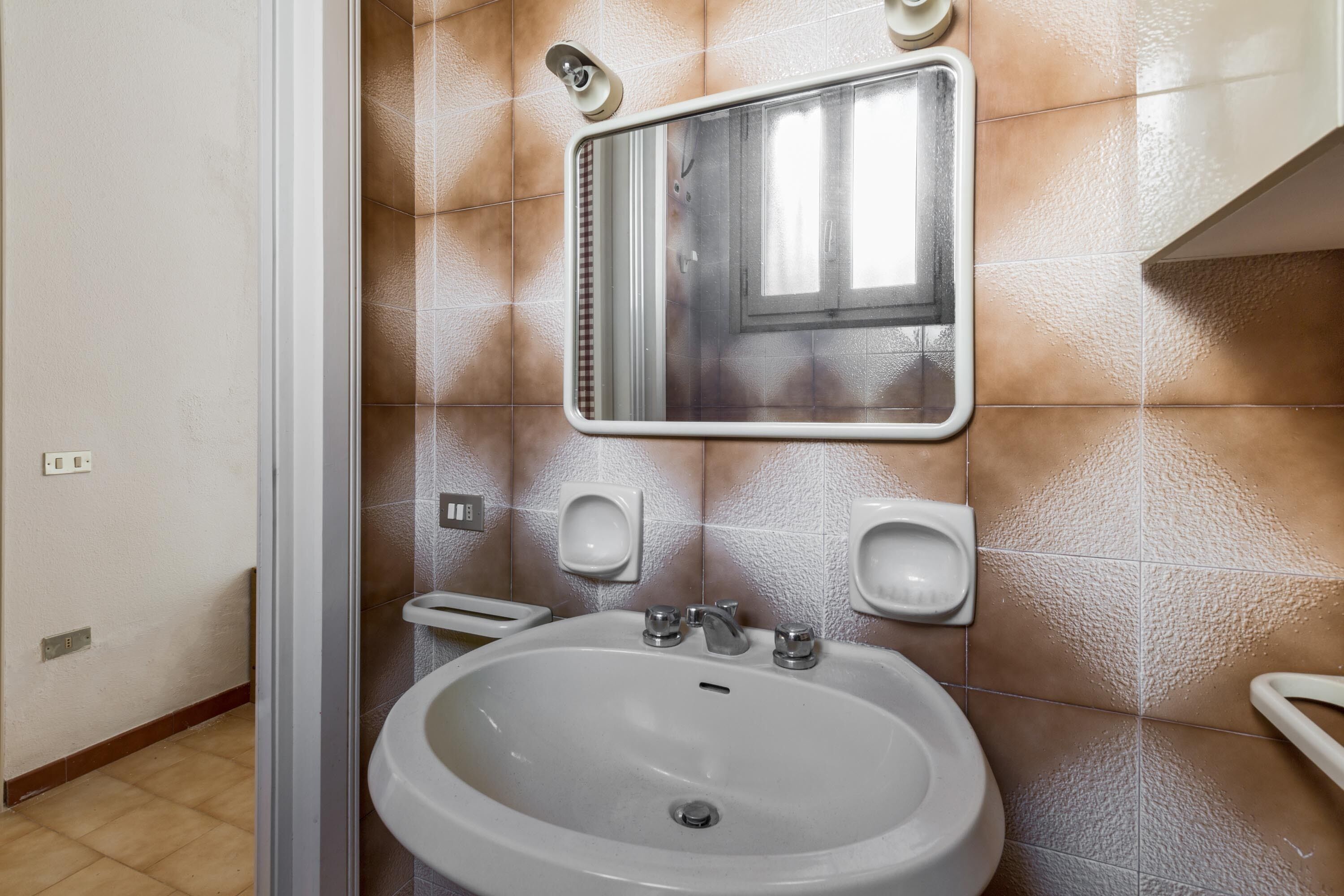 Un baño con lavamanos, espejo y dos dispensadores de jabón.