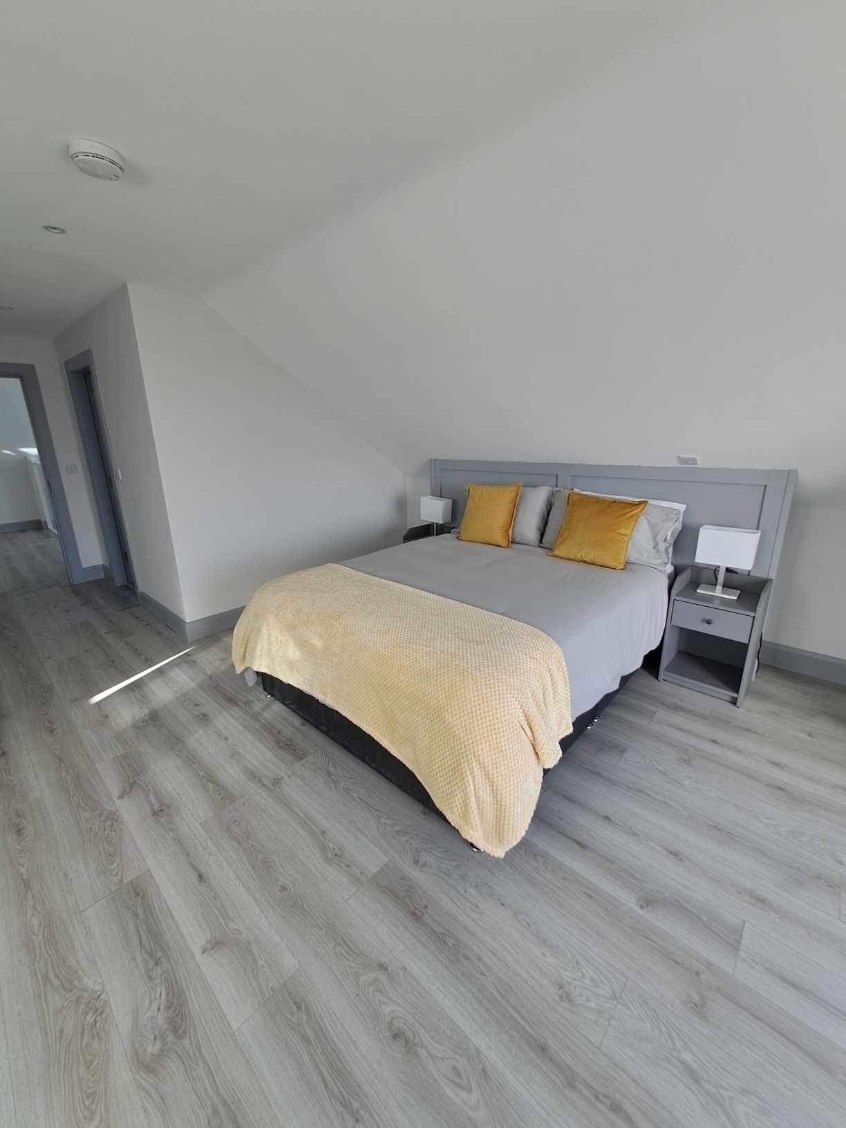 A modern bedroom with a bed, nightstands, and a wooden floor.