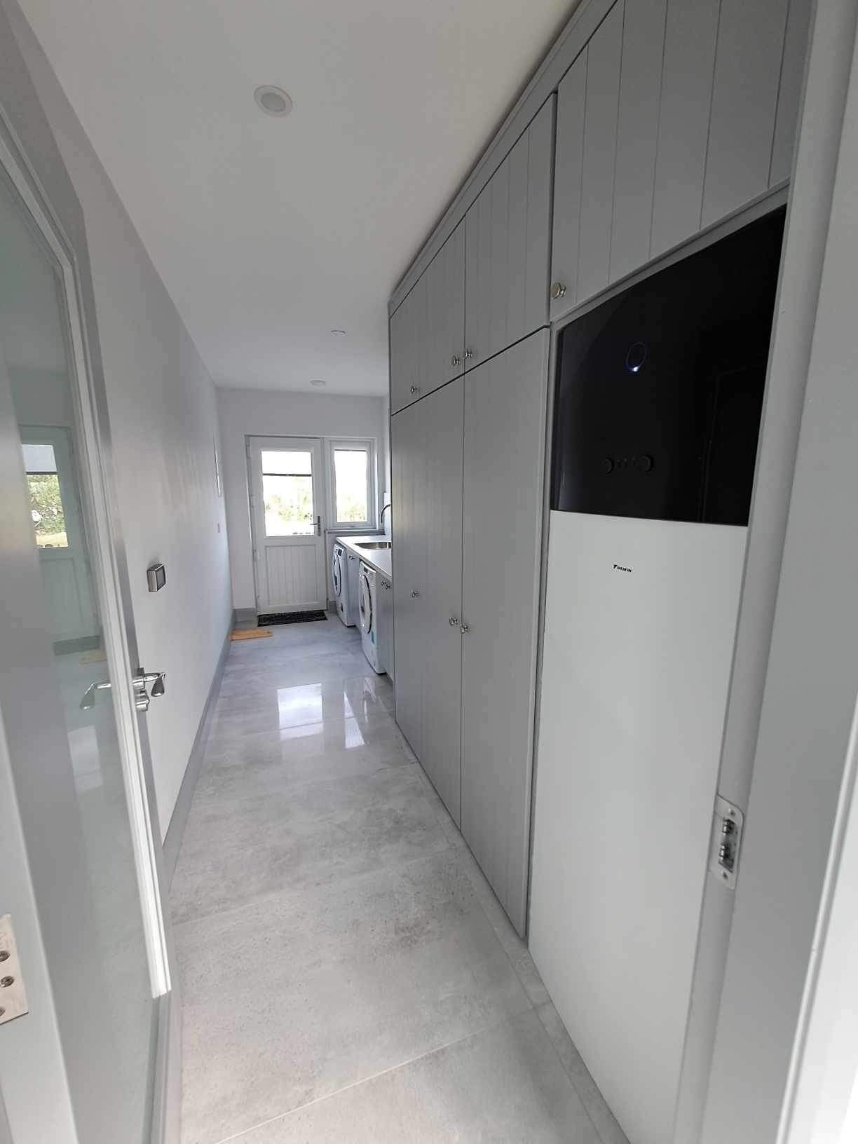 A narrow hallway with a washing machine and dryer, a door with a handle, and a light switch on the wall.