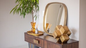 A wooden vanity with a mirror, a decorative vase, and a geometric sculpture. - Azalia Apartments (Sandton)