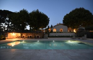 A pool area with a stone structure and a building with arched windows. - Domaine Perréal (Gargas)