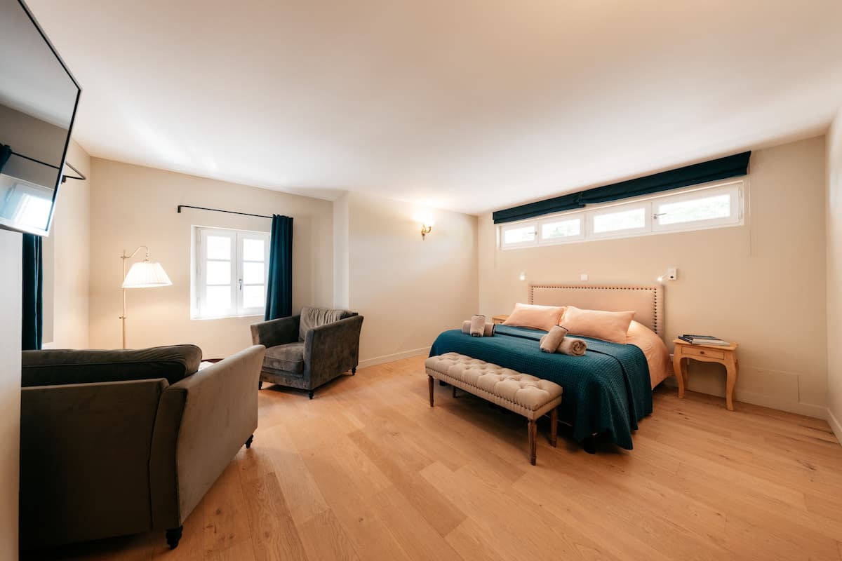 Quarto com cama, cadeira, banqueta, mesa de cabeceira e abajur.