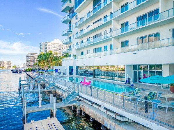 A waterfront hotel with a swimming pool, outdoor seating, and a dock.