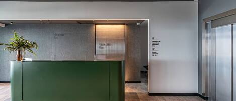 A modern reception desk with a green panel, a potted plant, and a glass partition labeled "FORUM CEAO".