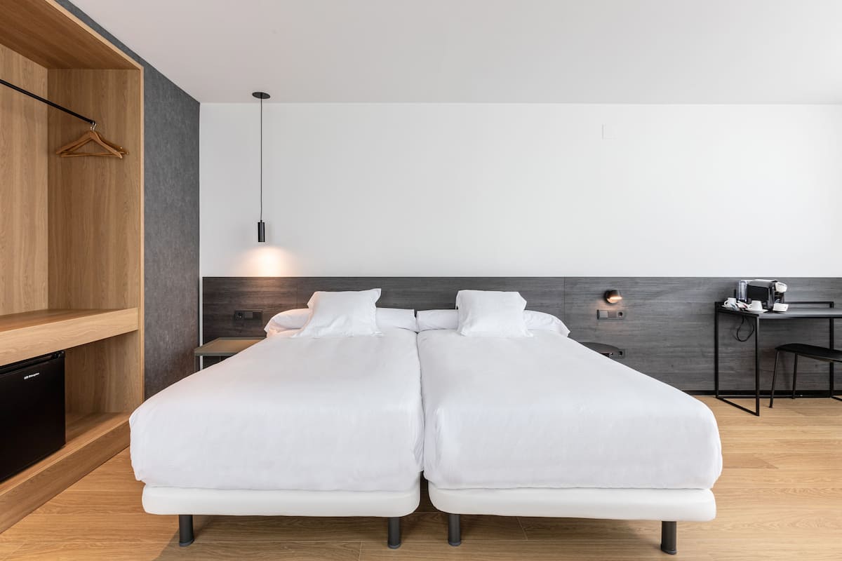 A modern hotel room with a double bed, a small desk with a coffee maker, and a hanging light fixture.