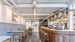 Un bar moderno con tavoli e sgabelli in legno, un bancone con attrezzature da bar e un cartello con la scritta "TABERNA DO MIÑO".