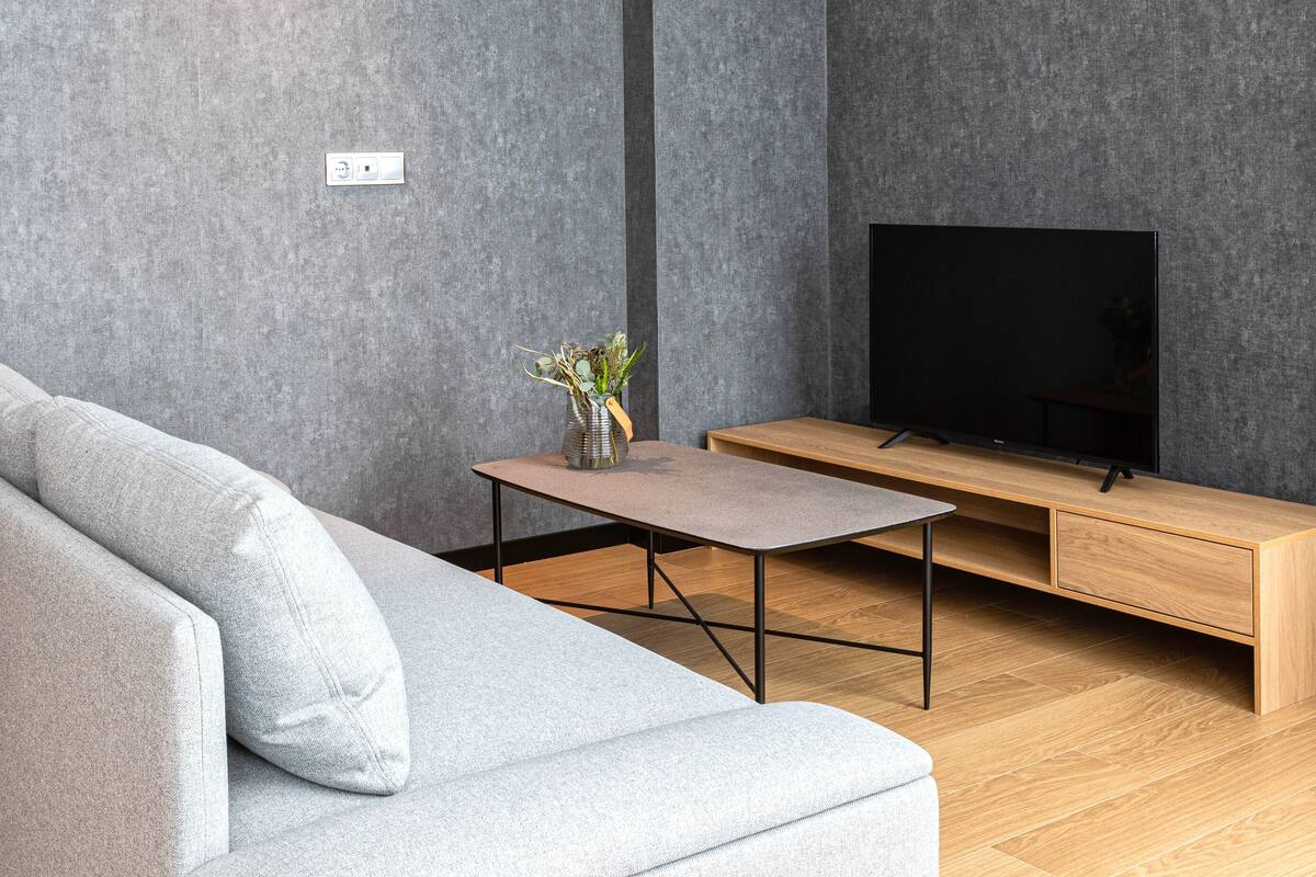 A modern living room with a grey sofa, a wooden coffee table, and a TV on a wooden stand.