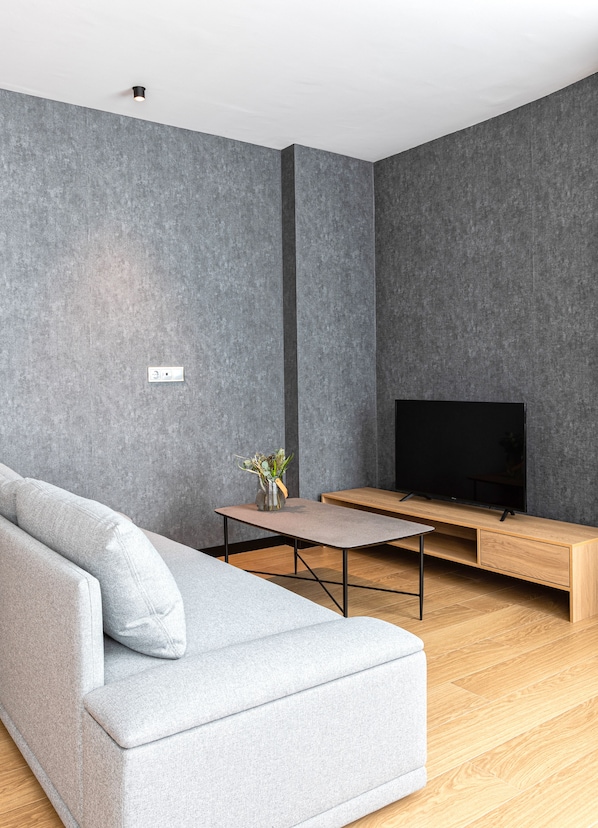 Una sala de estar moderna con un sofá gris, una mesa de centro de madera y un televisor sobre un mueble de madera.