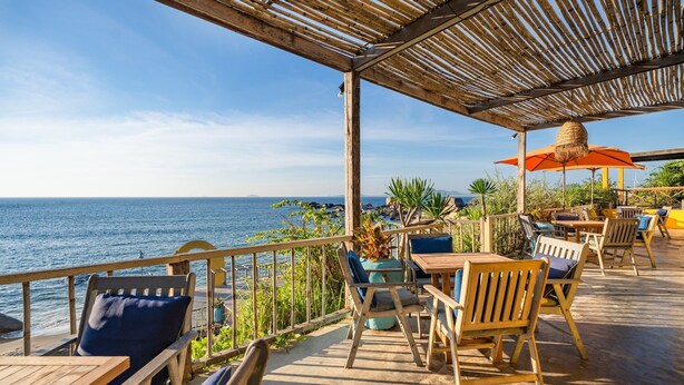 An outdoor seating area with wooden furniture and a view of the sea. -  Life Resort Quy Nhon (Cat Tien)
