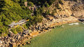 An aerial view of a coastal area with a rocky beach, clear waters, and a building with a sloped roof. -  Life Resort Quy Nhon (Cat Tien)