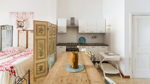 A compact kitchen with white cabinets, a stove, and a sink. A wooden table with a vase of flowers is in the center. - 3821 VBR - Mono Rosa by Barbarhouse (Porto Cesareo)