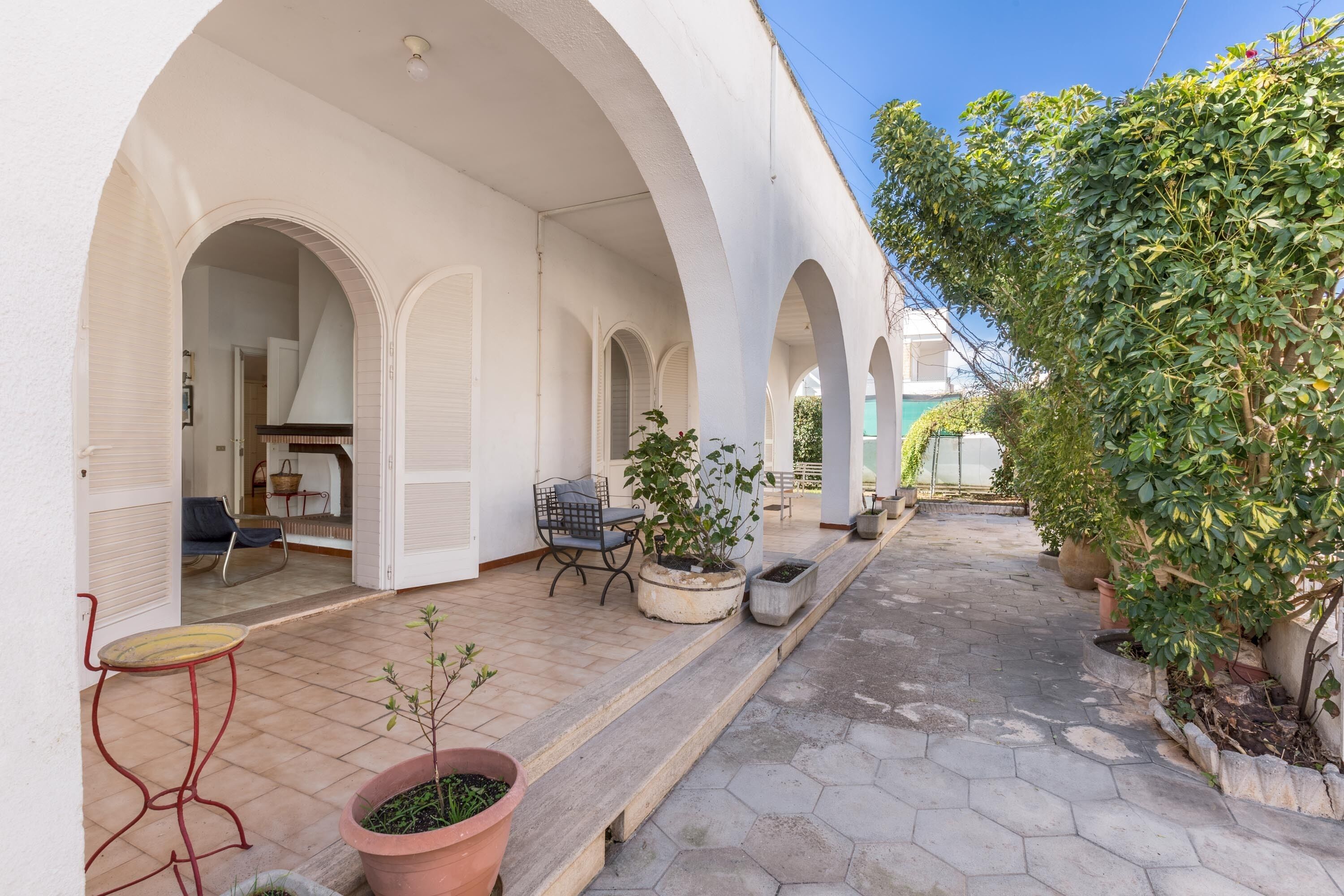 A covered outdoor area with a tiled floor, potted plants, and a seating area with a table and chairs.