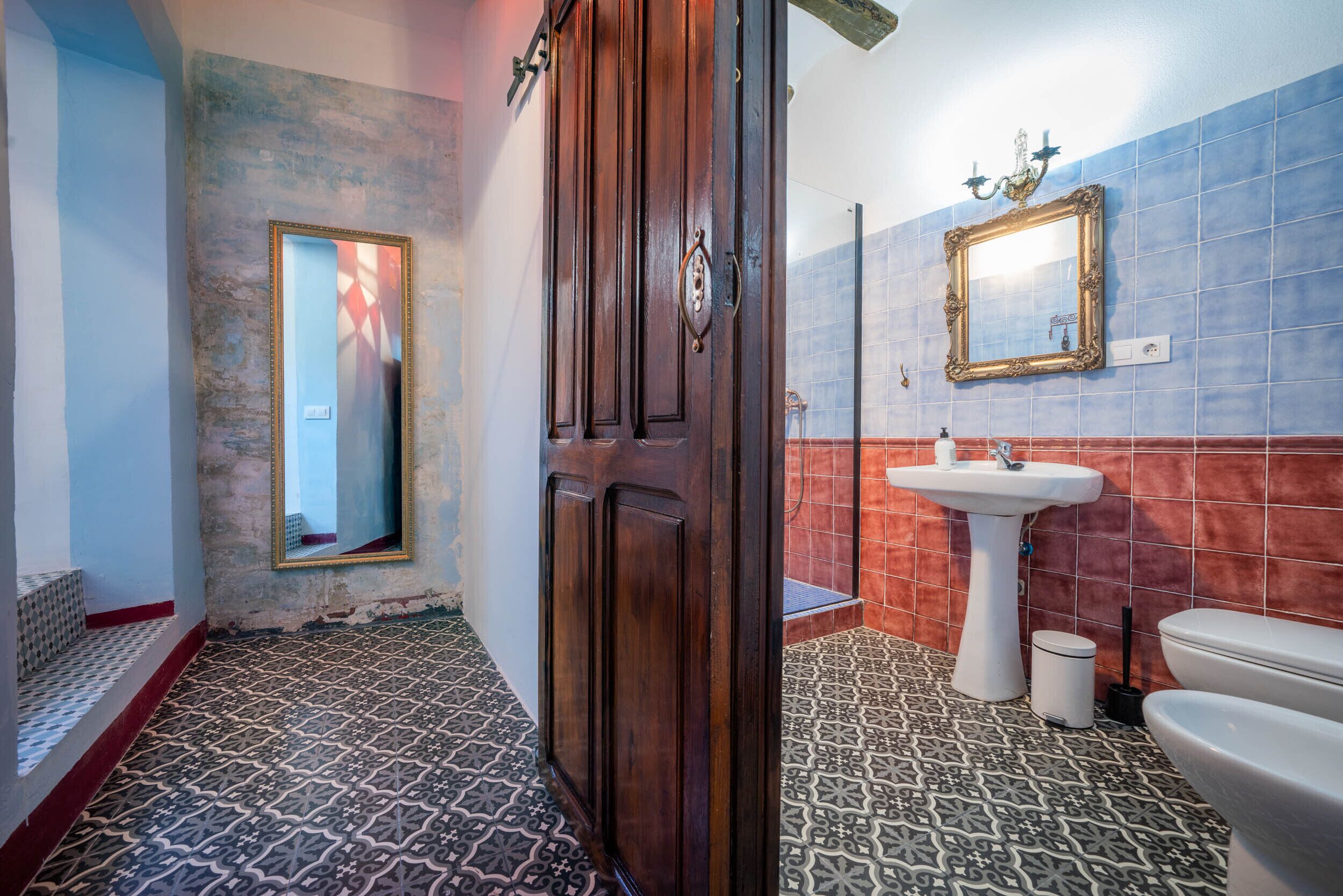 A bathroom with patterned floor tiles, a wooden door, a mirror, a sink, and a toilet.