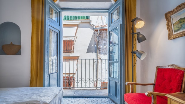 A room with a bed, a red chair, a table, a lamp, and a view of the outside balcony. - 7 Pisos Casa Rural de Pueblo (Cocentaina)