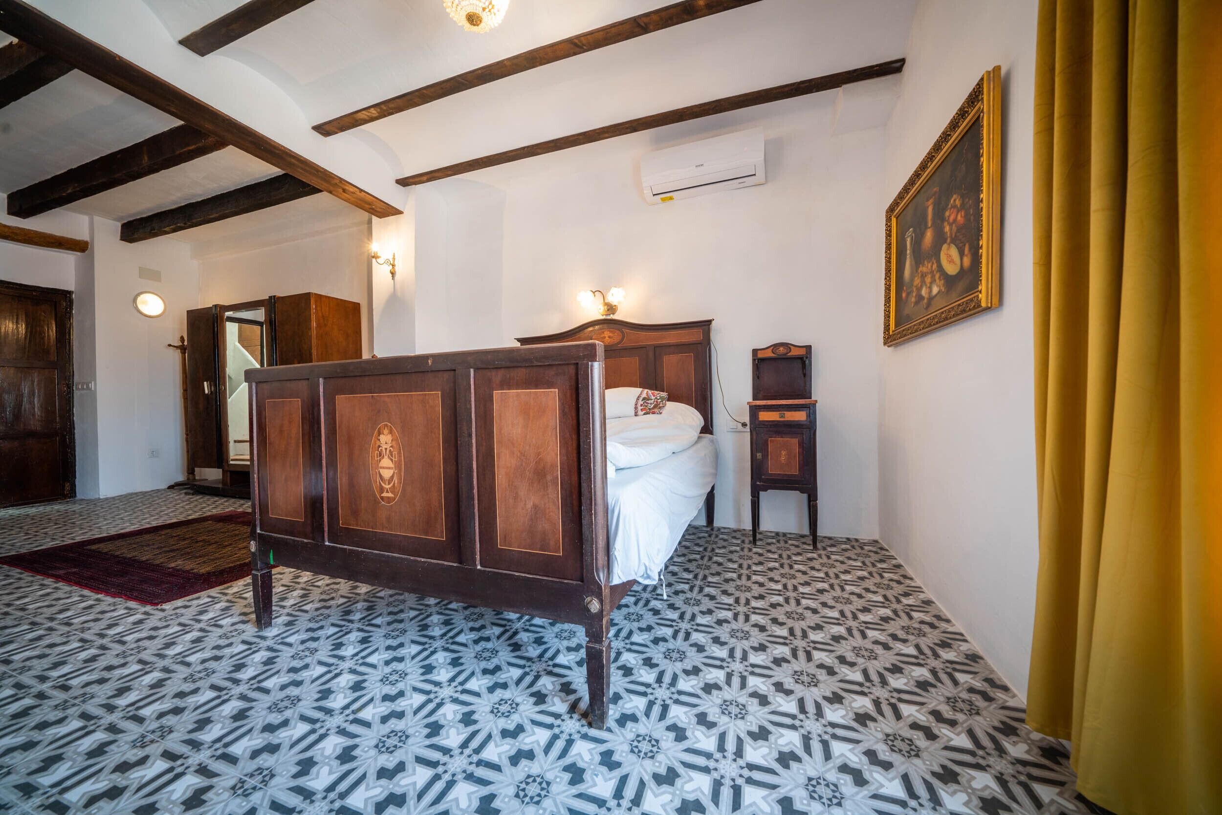 Un dormitorio con cama de madera, piso estampado y un cuadro en la pared.
