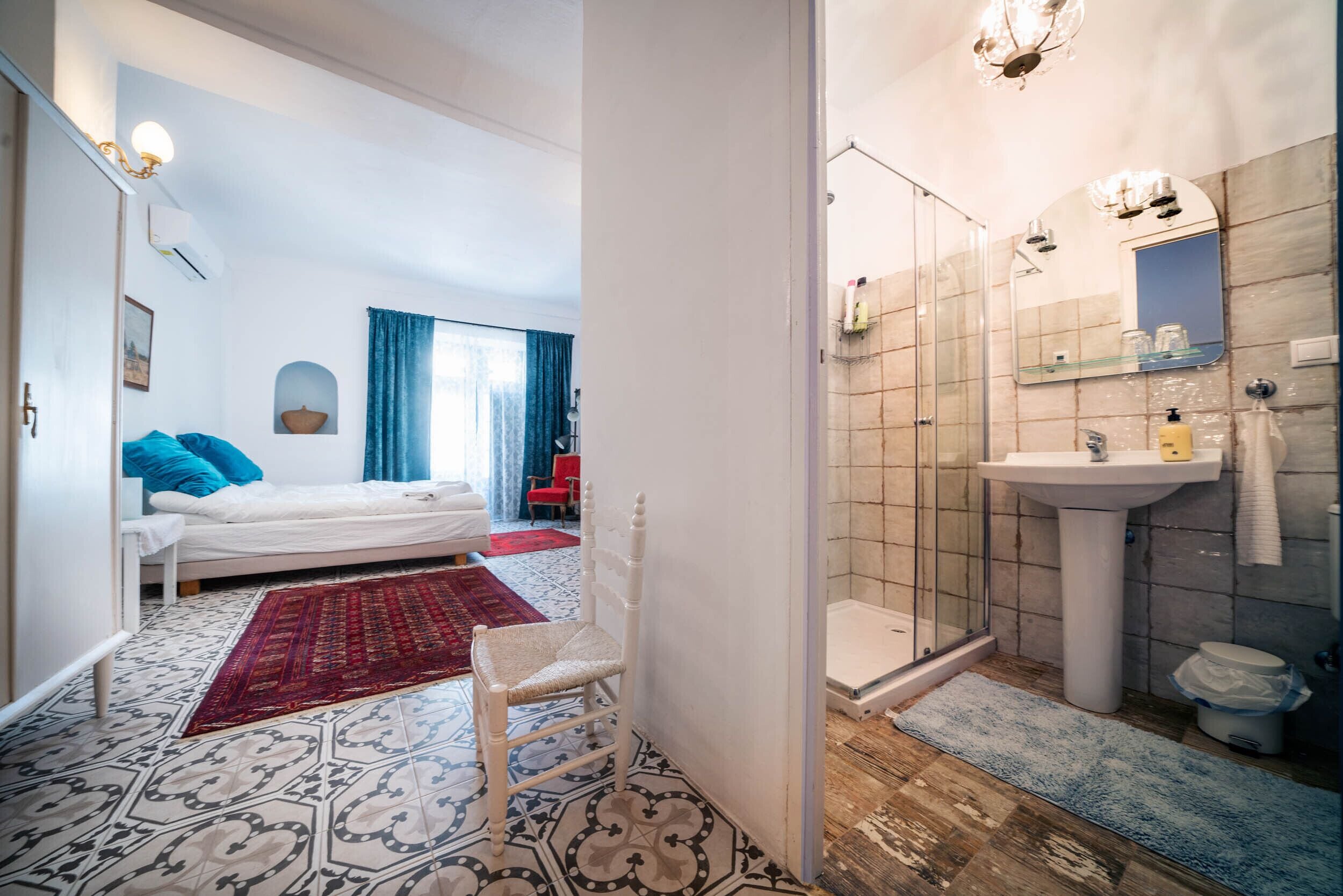 A bedroom with a bed, a chair, a red rug, and a bathroom with a sink and shower.