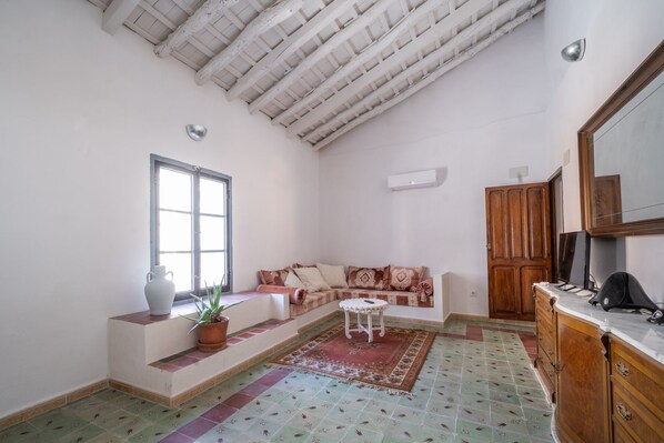A spacious living room with a high ceiling, a large window, a sofa, a small table, a cabinet, and a television.