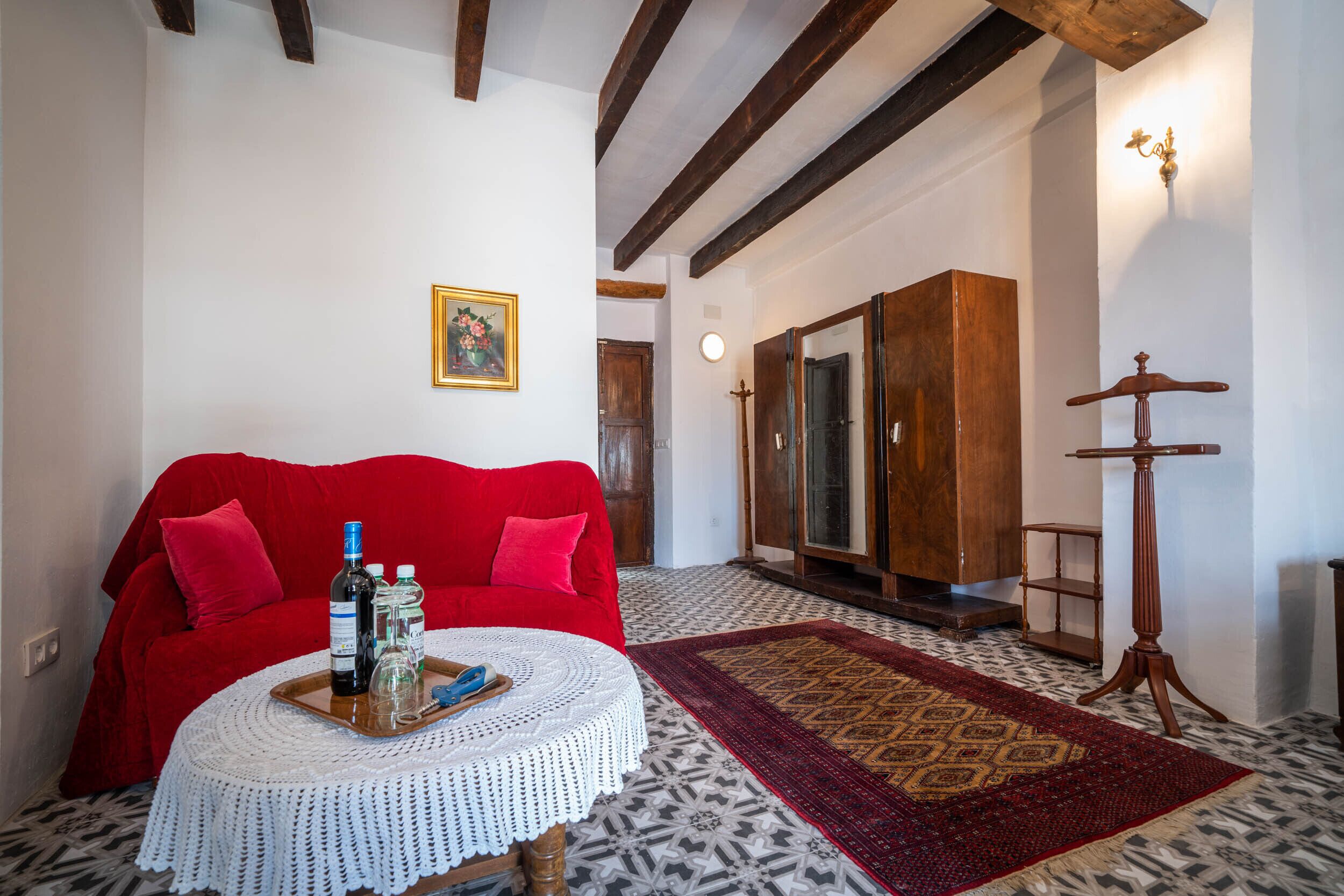 A living room with a red sofa, a round coffee table with drinks, a patterned rug, and a wooden cabinet.
