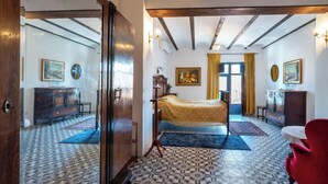 A room with a bed, wooden beams, a patterned floor, and a red chair. - 7 Pisos Casa Rural de Pueblo (Cocentaina)