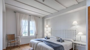 Un dormitorio con dos camas, una silla, un escritorio y una ventana con cortinas.