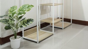 A white metal shelving unit with wooden hangers and a potted plant beside it. - 2B Cozy Hostel (Trang)