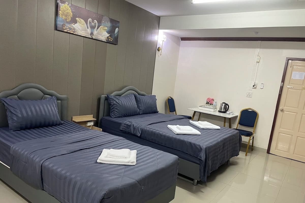 A hotel room with two beds, a small table with a kettle, and a chair.
