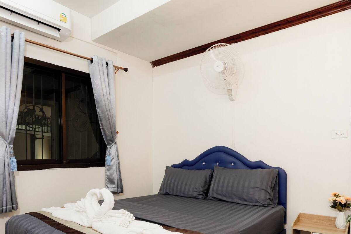 A bedroom with a large bed, a bedside table, a nightstand, an air conditioning unit, and a window with curtains.