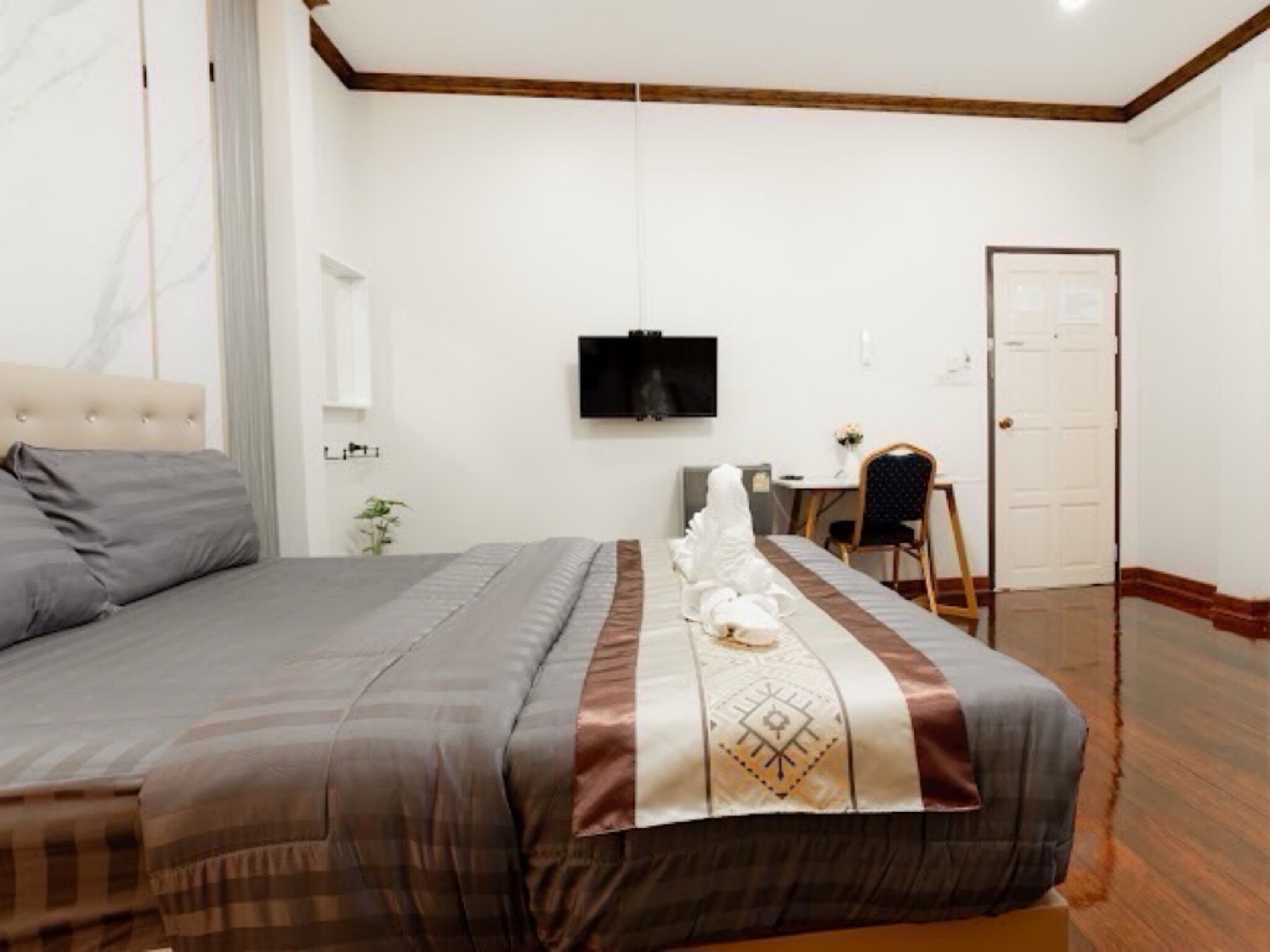 A neatly arranged bedroom with a bed, a television mounted on the wall, a small table with a chair, and a door.