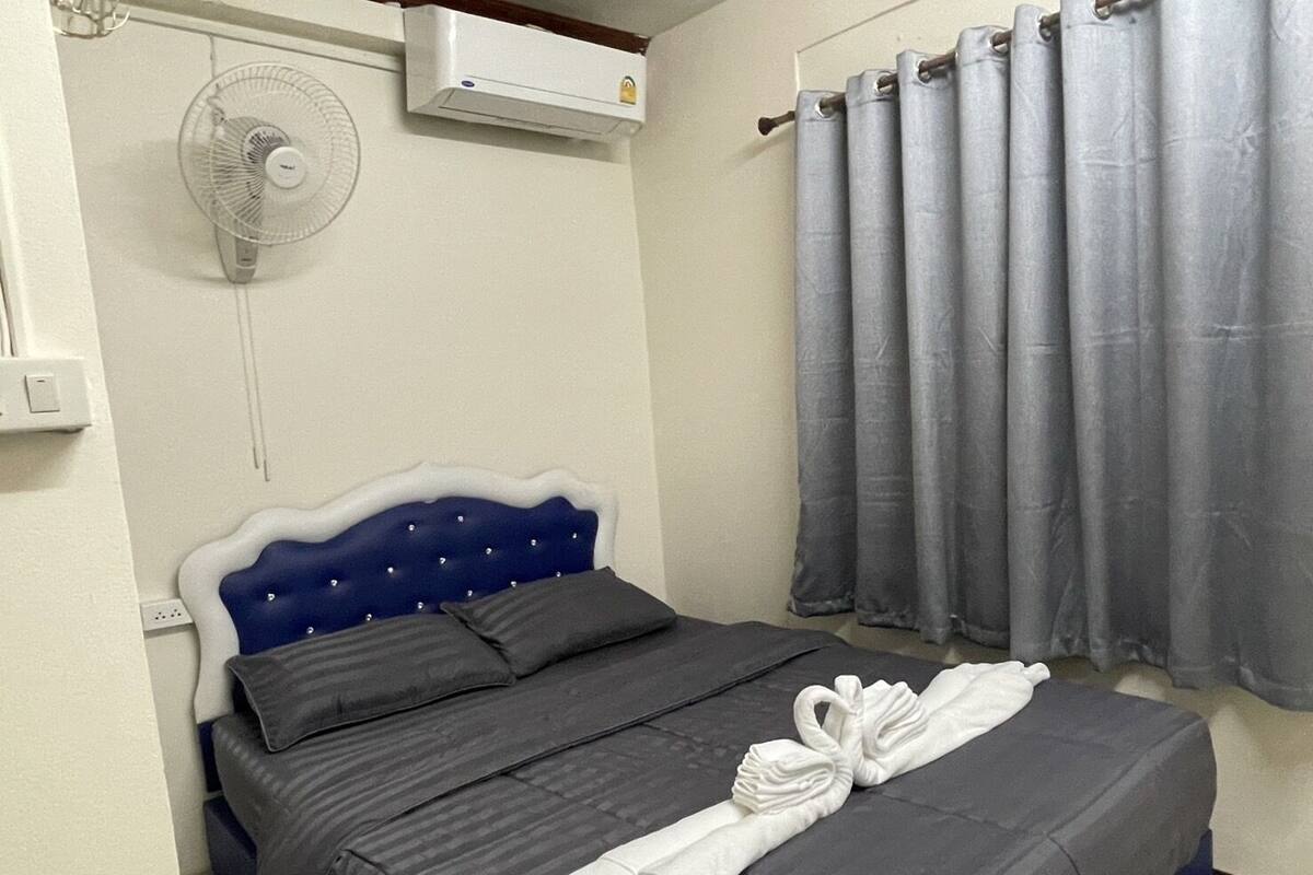 A bedroom with a bed, a wall-mounted air conditioner, a ceiling fan, and grey curtains.