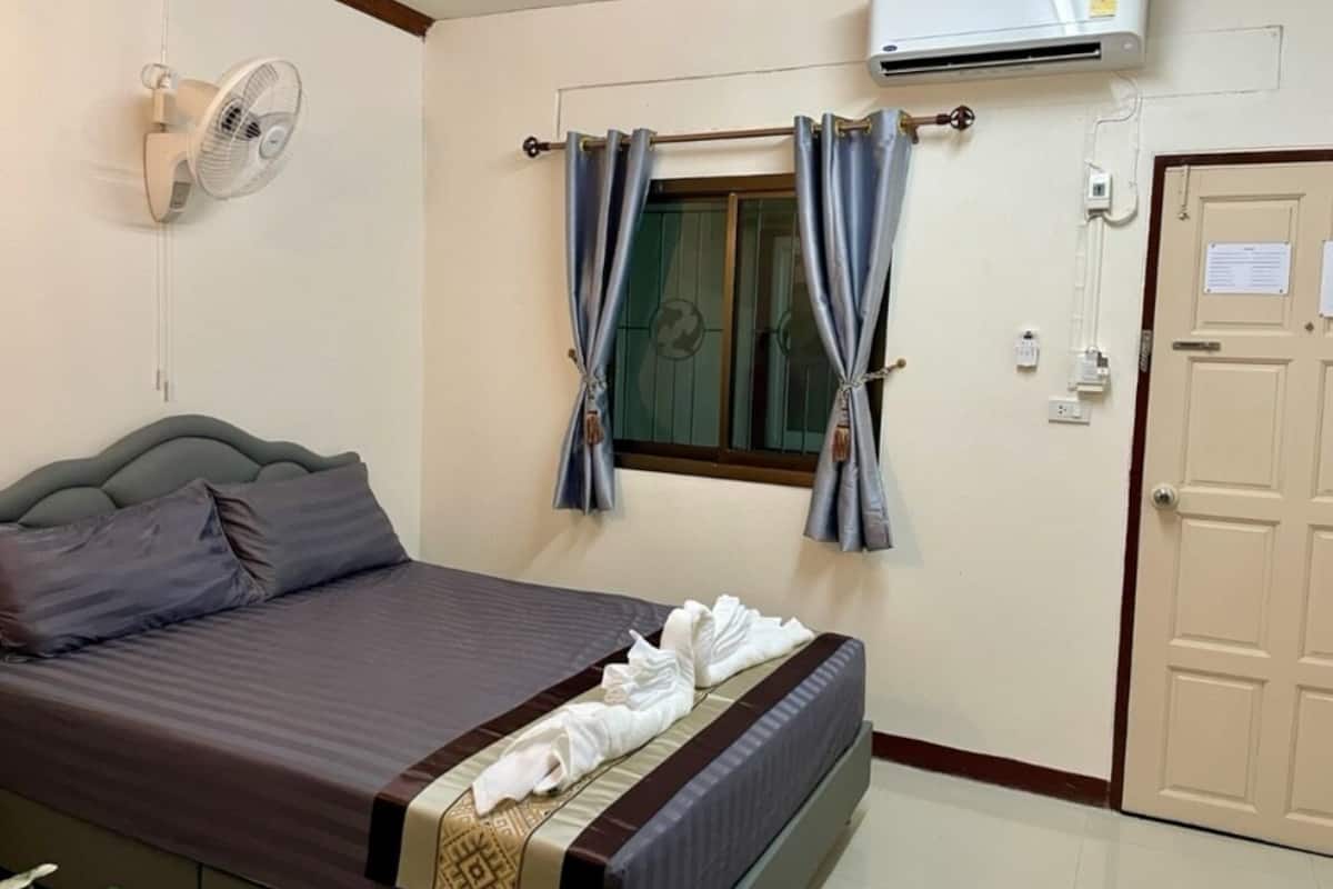 A hotel room with a bed, a wall-mounted air conditioner, a window with curtains, and a door.