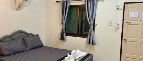 A hotel room with a bed, a wall-mounted air conditioner, a window with curtains, and a door.