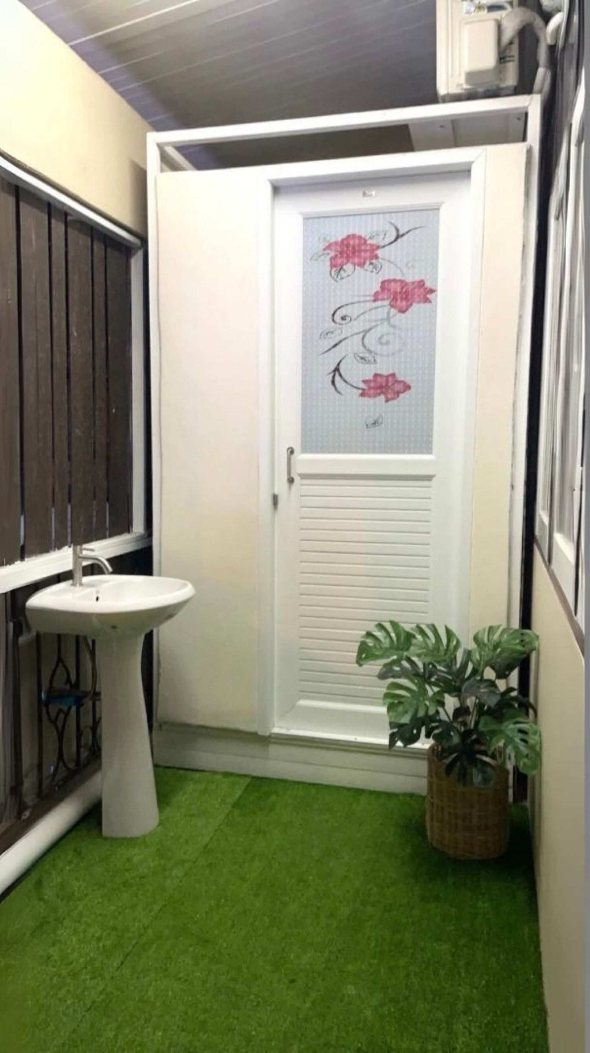 A small bathroom with a white door, a white sink, and a green artificial grass floor.