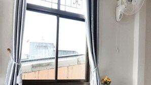 A room with a window, a white table, a chair, a fan, and a vase with flowers. - 2B Cozy Hostel (Trang)