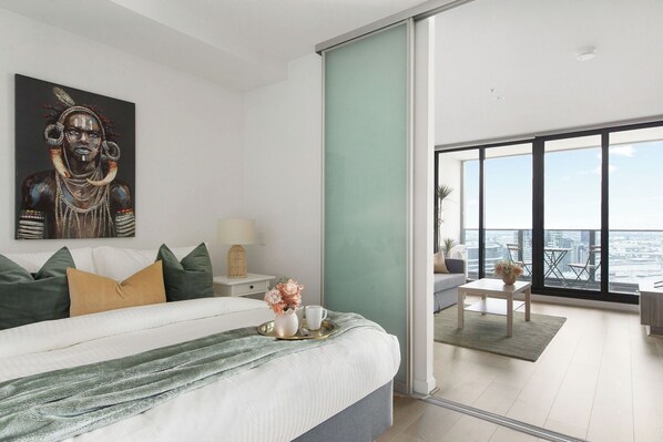 A modern bedroom with a large bed, a city view balcony, and a painting on the wall.