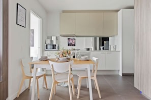 A modern kitchen with white cabinetry, a wooden dining table, and four chairs. - A Cozy 2BR Apt with Harbour Views, FREE Parking (Melbourne)