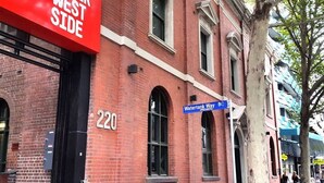 A red brick building with a sign reading "Upper West Side" and a blue street sign for "Watertank Way."