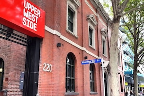 A red brick building with a sign reading "Upper West Side" and a blue street sign for "Watertank Way." - A Cozy 2BR Apt with Harbour Views, FREE Parking (Melbourne)