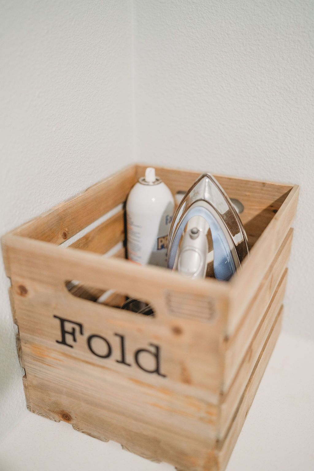 A wooden crate with the word "Fold" on it, containing a spray bottle and a metal object.