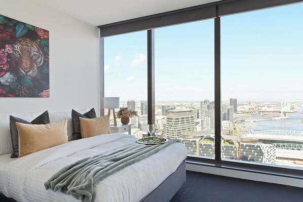 A modern bedroom with a large bed, a city view, and a tiger painting on the wall.