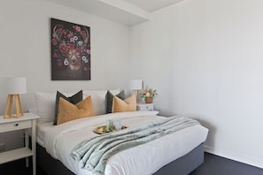 Un dormitorio moderno con una cama, mesitas de noche, lámparas y un cuadro en la pared.